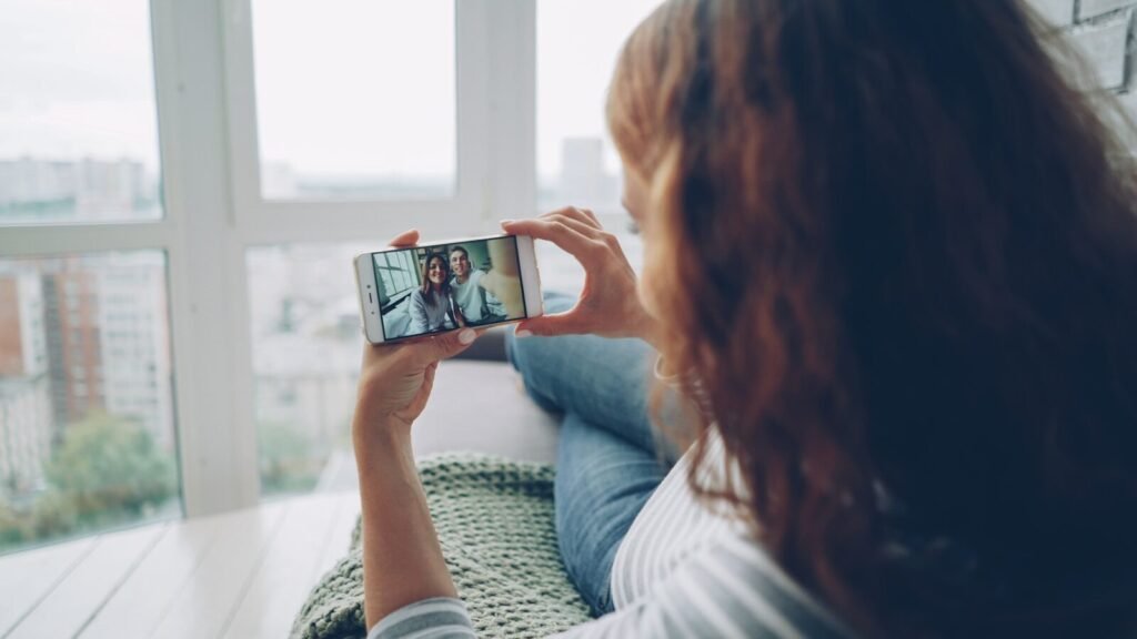 Woman holding phone watching video call by window